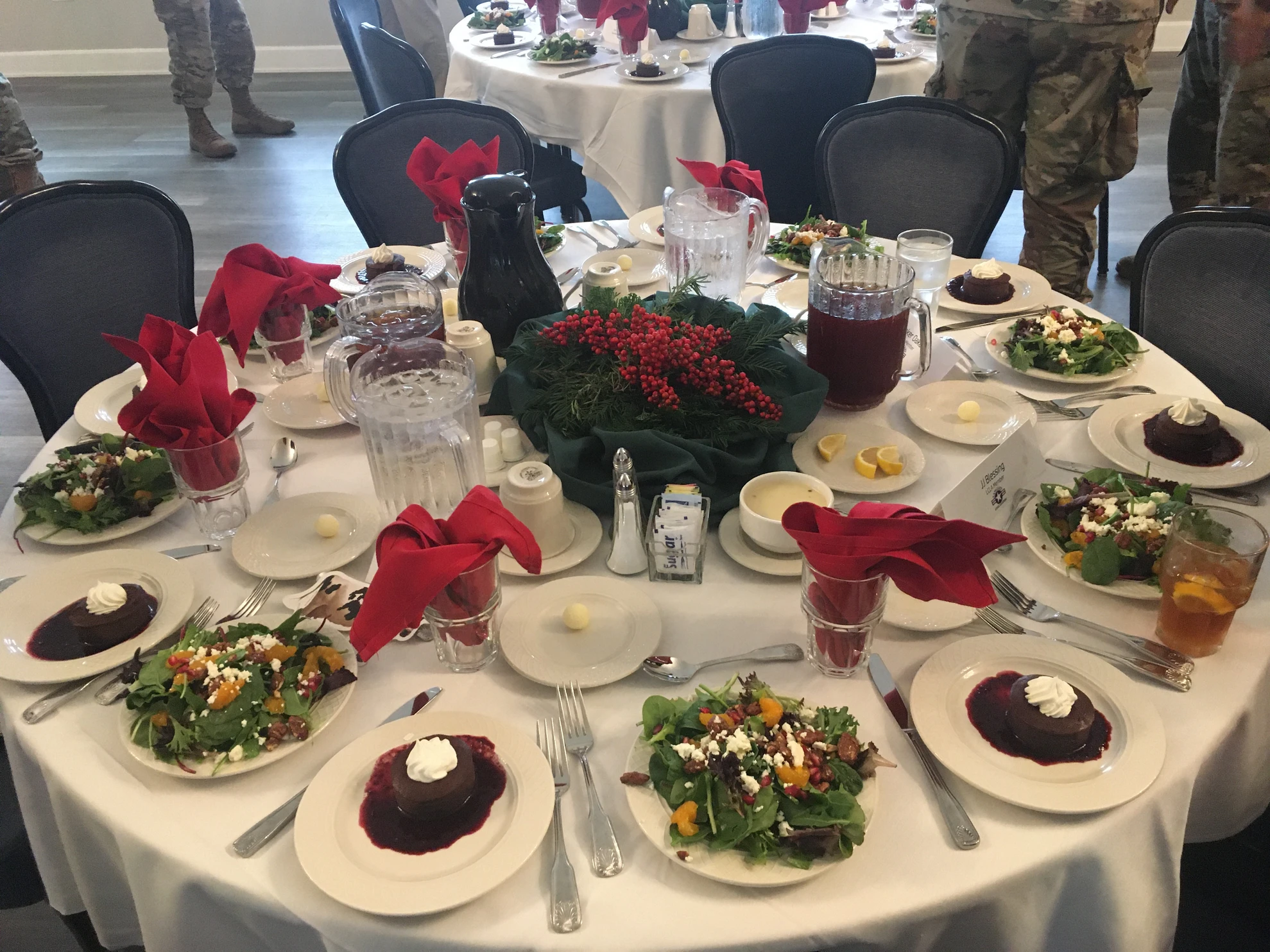 Round table with red napkins, holly centerpiece, desserts and salads