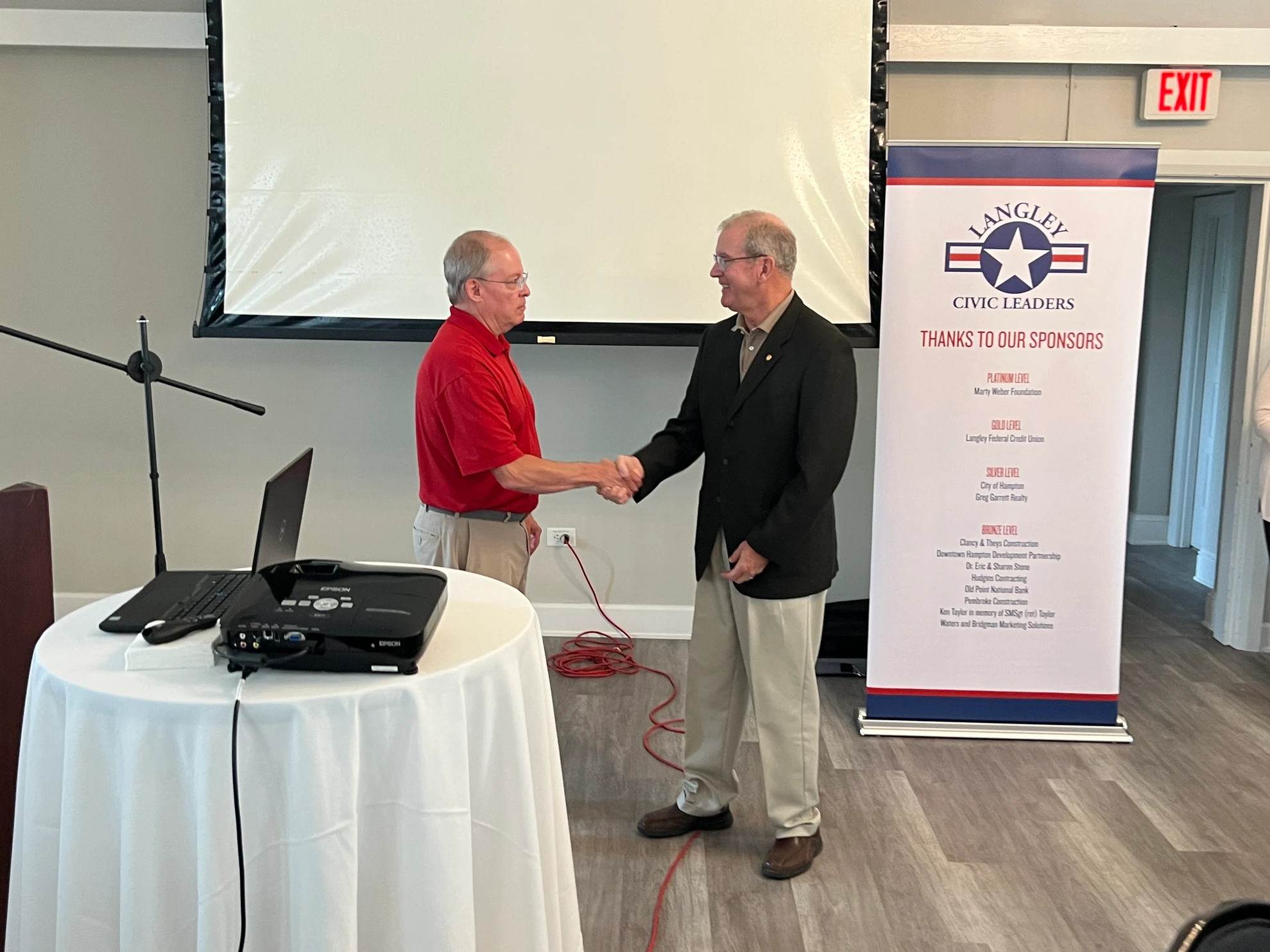 Two members shaking hands in front of LCLA sponsors banner
